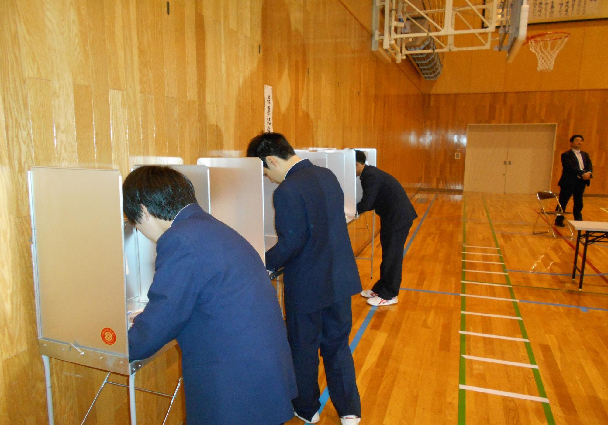 記載台で投票用紙に記名する生徒